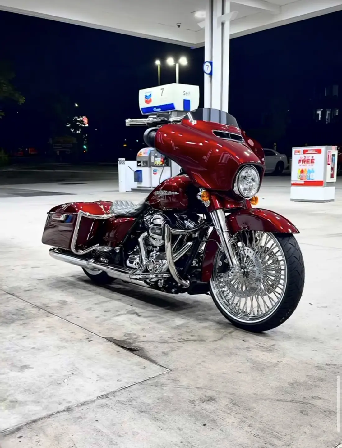 2025 custom Harley bagger in candy red, parked under the lights of a gas station at night